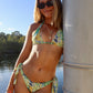 Woman in a floral bikini leaning against a pole by a body of water.